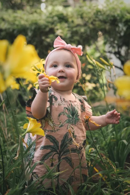 Young child holding a yellow flower in a garden